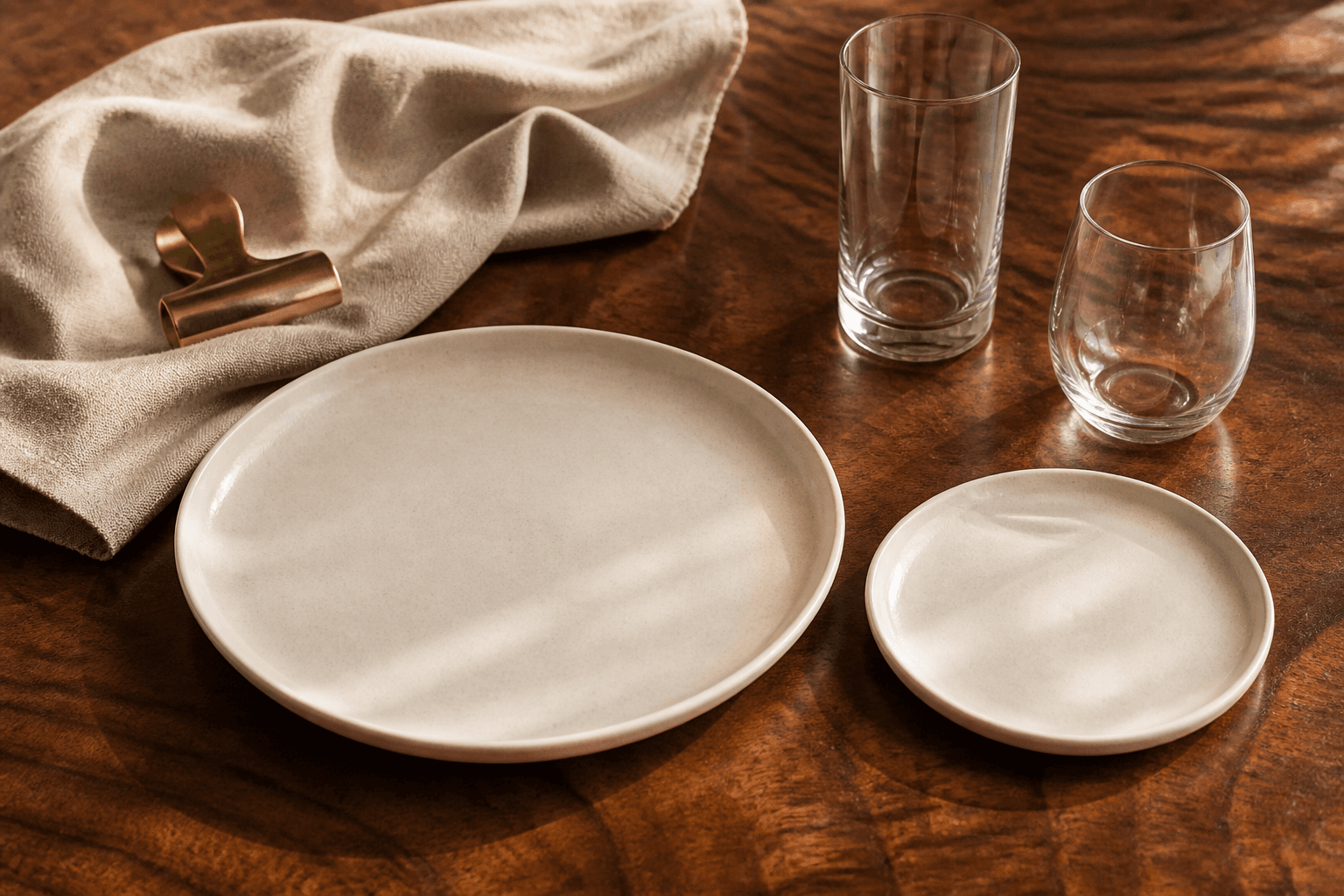 One unused adult ivory plate beside one smaller unused ivory child’s plate on a koa table, brass clip.