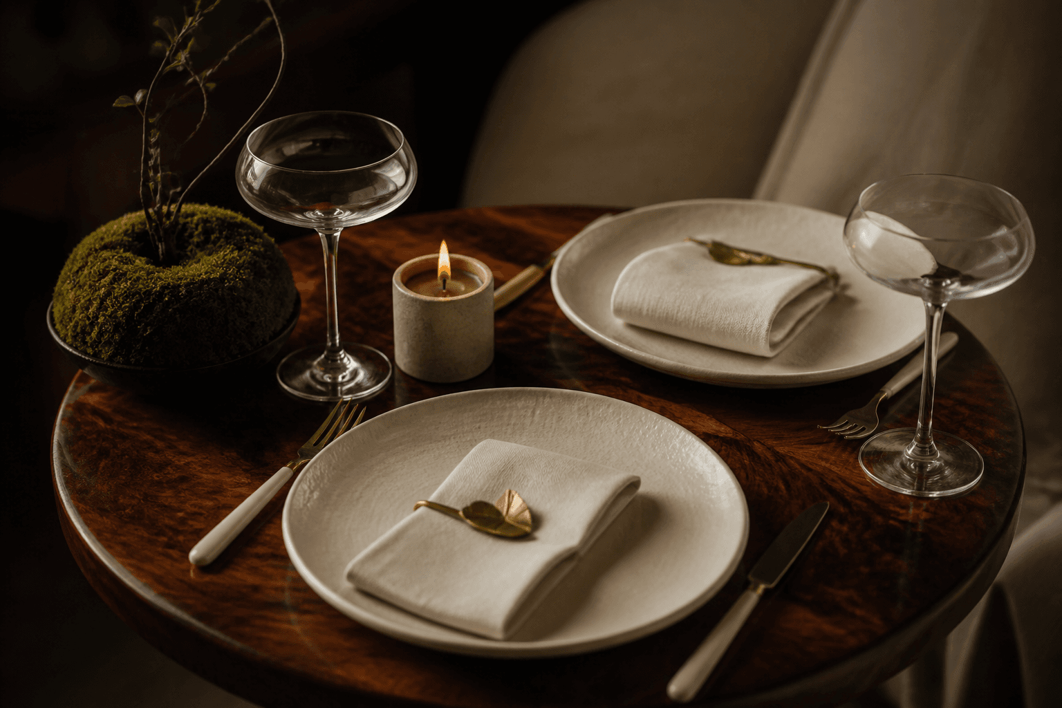 Two unused ivory place settings close together on a small koa table, two empty coupes, unlit candle.