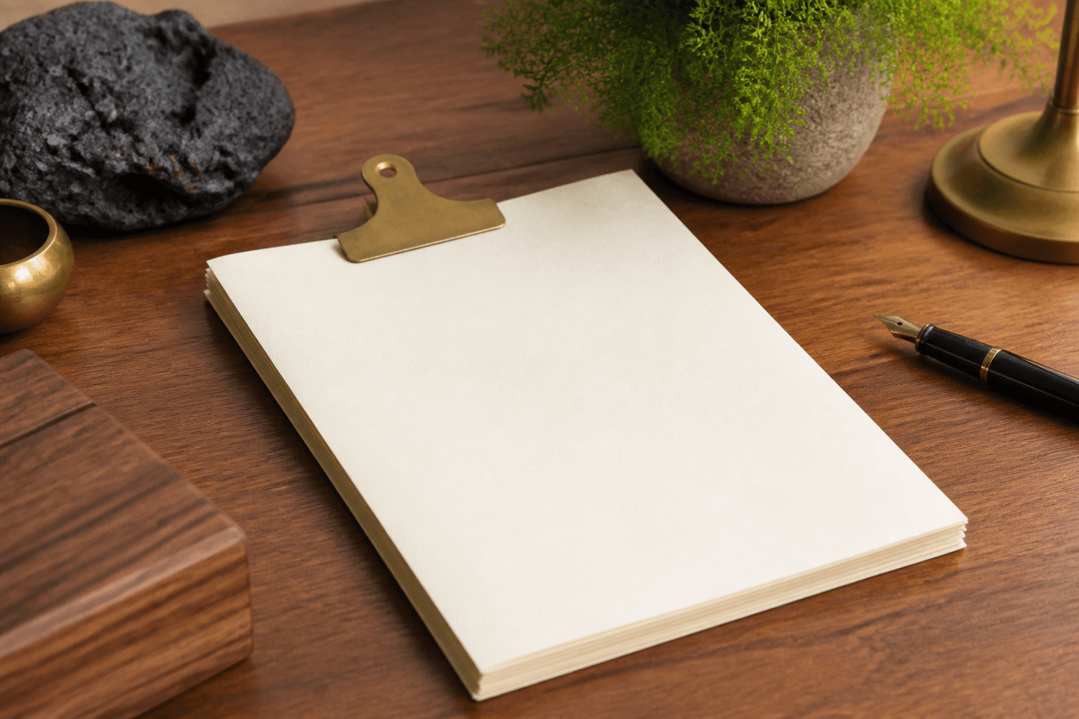Unmarked unused ivory papers under a brass clip on a koa desk, fountain pen, no numbers.