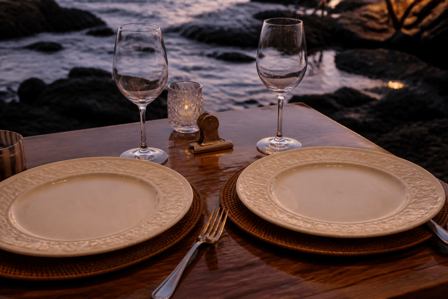 Two unused ivory place settings close together on a small koa table, brass clip.
