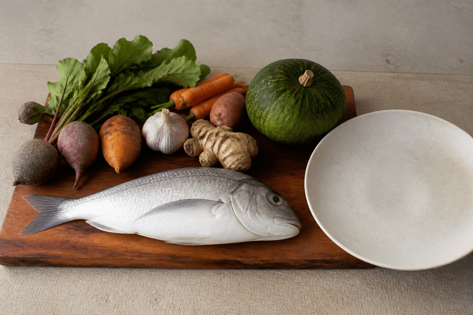 Unmarked whole produce and a whole fish on a koa board, unused ivory plate, no labels.
