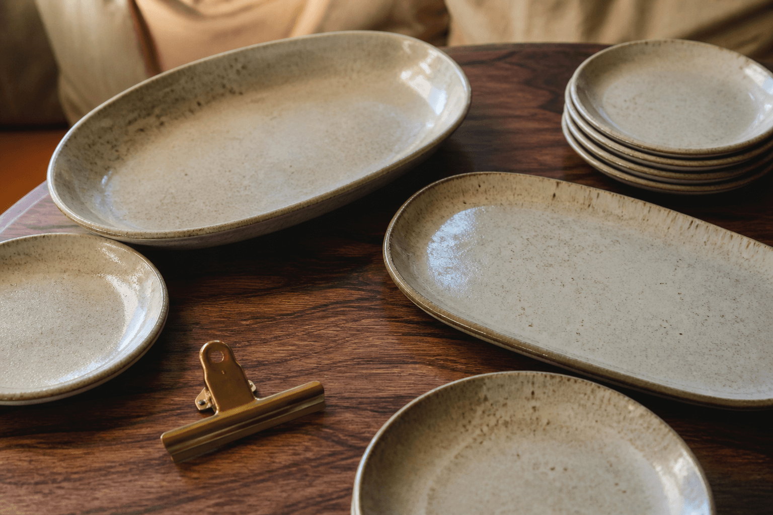 Unused empty shared platters and unused ivory plates on a koa table, brass clip.